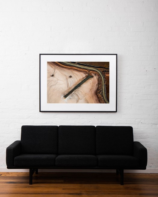 A horizontal abstract , aerial photo of Australian Landscape in green and brown framed on black timber on white wall above sofa