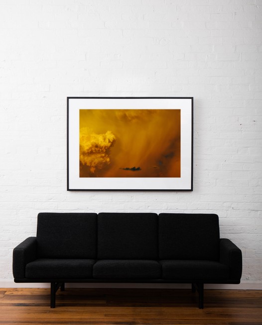 A Large horizontal photo of Australian Landscape in a Summer afternoon with orange and yellow clouds framed in black timber on white wall above sofa