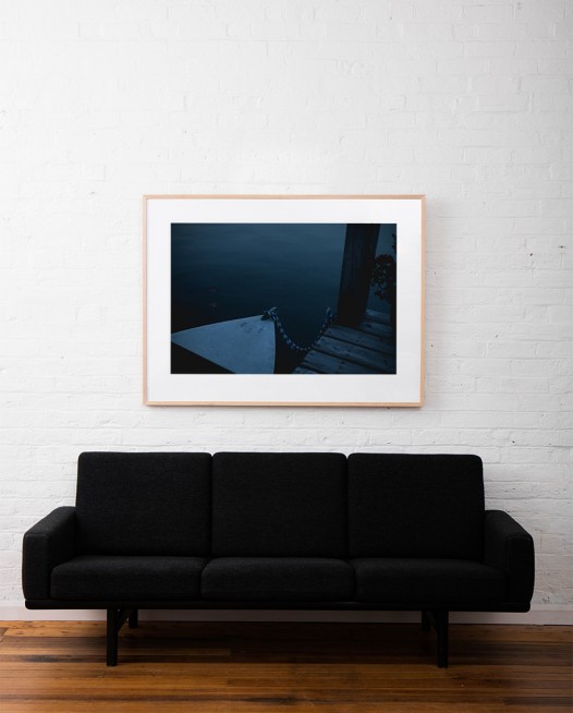 A horizontal Landscape photo of a boat tied to jetty framed in raw timber on white wall above sofa