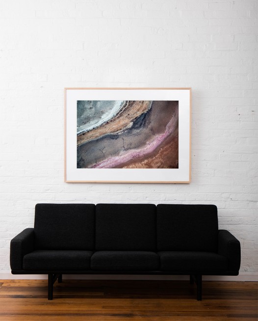 A horizontal abstract, aerial photo of Australia water in pink, purple, and red framed in raw timber above sofa