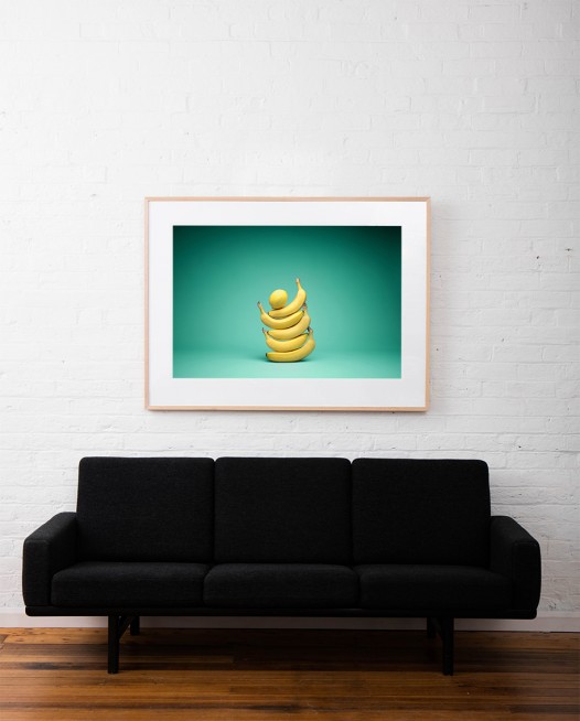 Large Still Life photo of a lemon on top of 5 bananas framed in raw timber on white wall above sofa