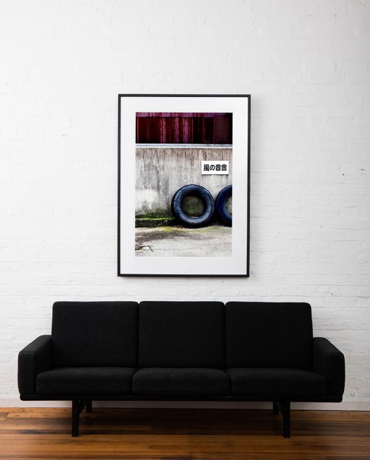 A large vertical abstract photo of 2 wheels taken in Urban Japan. Framed in black timber on white wall above sofa