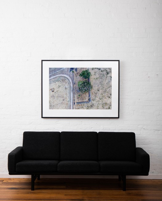 A Large Abstract Aerial photo of Australian Landscape of tress, road and paddocks framed in black timber on white wall above sofa