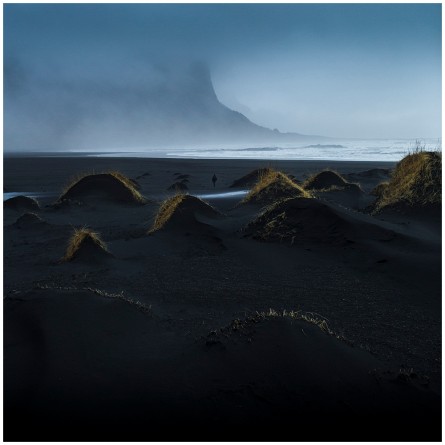 A Icelandic landscape art photograph of sea and beaches with misty mountains background. there is lone person walking on the beach