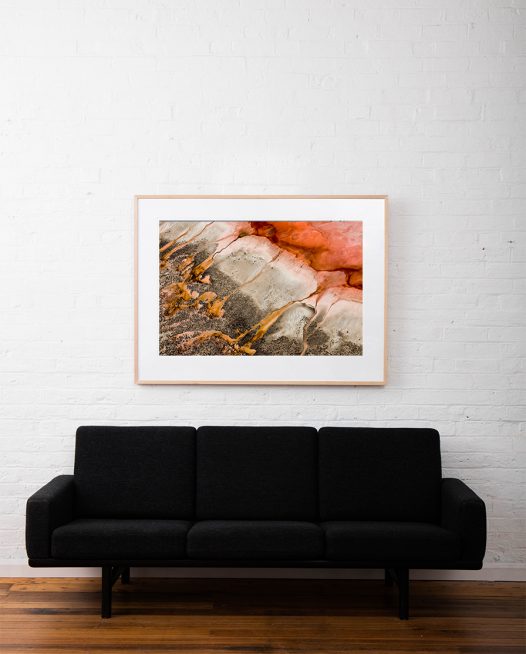 Red and gold aerial photo of the Western Australian landscape print framed in timber frame on white wall above sofa