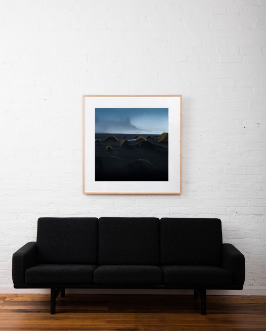 A misty photographic image of icelandic landscape of beaches, sea and mountains in shades of blue framed in raw timber on wall above sofa