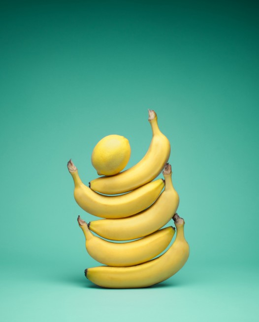 Still Life photo of a lemon on top of 5 bananas.