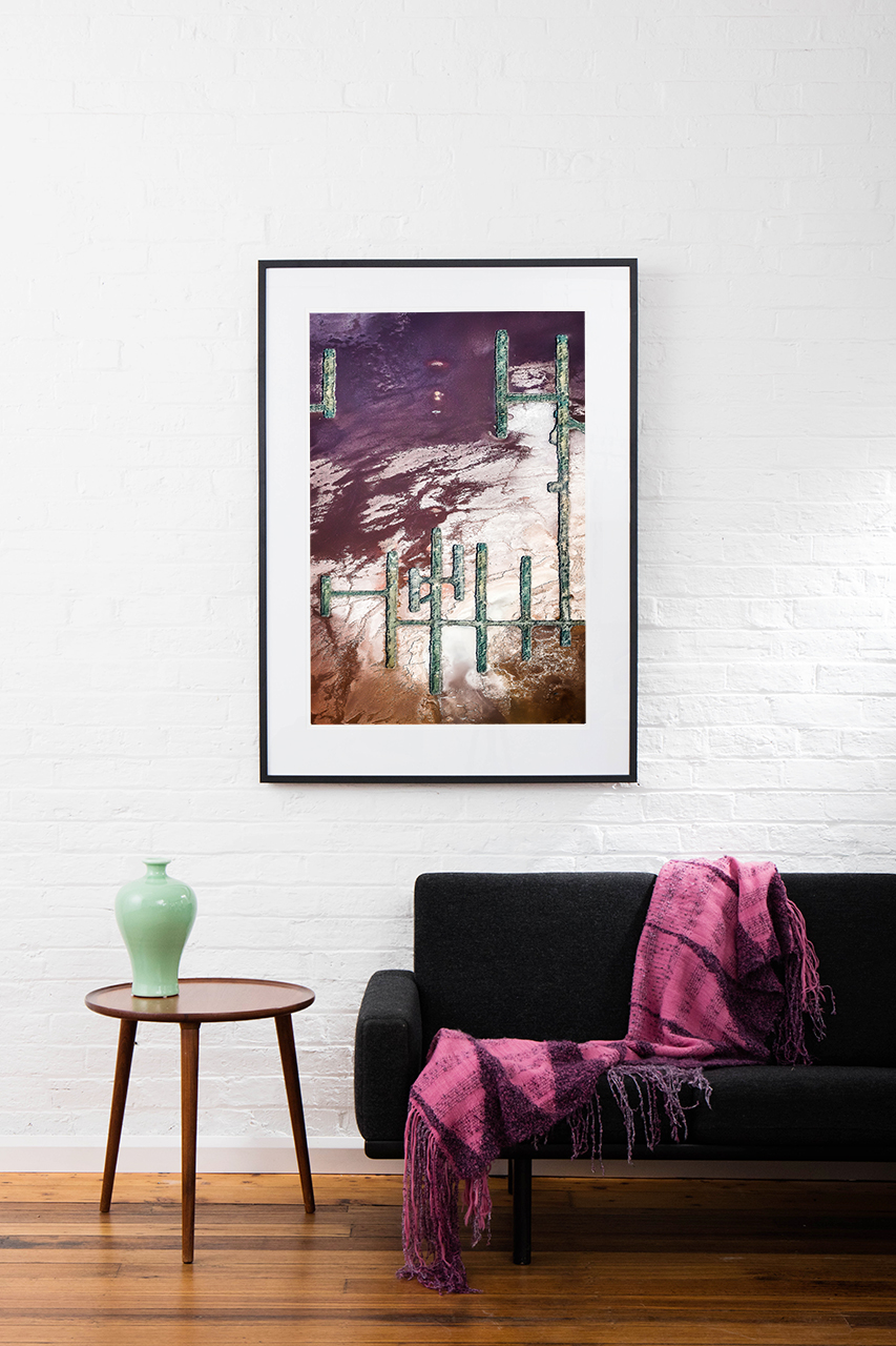 A Vertical Abstract Aerial photo of Australian Landscape in Pink, Purple and Red framed in dark timber on wall in living room