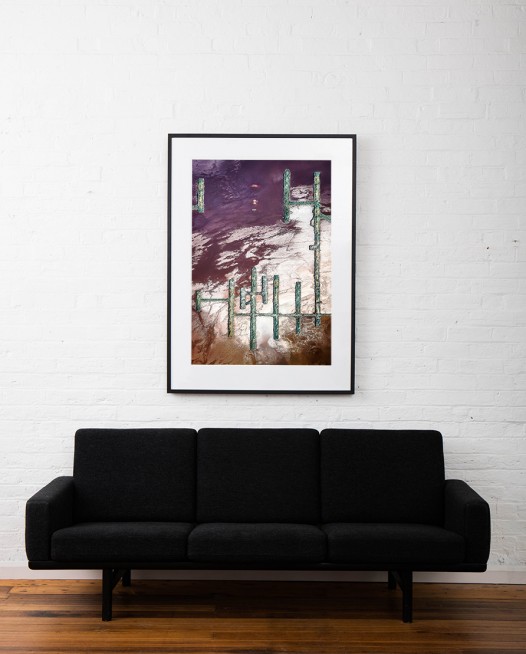 A Large Vertical Abstract Aerial photo of Australian Landscape in Pink, Purple and Red framed in black timber on white wall above sofa