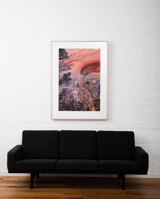 A Large Vertical Abstract Aerial Landscape photo of water in orange, pink, black and red taken in Australia framed in raw timber on white wall above sofa