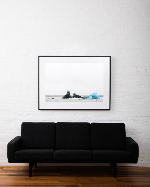 Large photographic art image of glacier, iceberg floating in water taken in Iceland Landscape. Framed in black timber on white wall above sofa