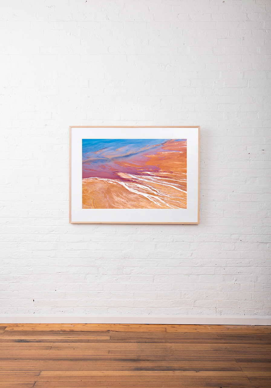 A large Abstract Aerial Landscape photo taken in Shark Bay, Australia with splash of colour in orange pink and blue framed raw timber on white wall