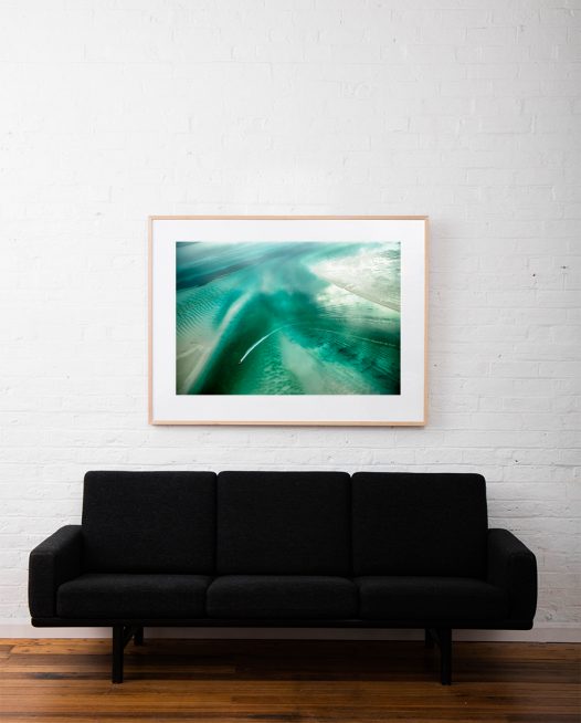 A Large Abstract Aerial Landscape photograph of water in green and white framed in raw timber on white wall above sofa