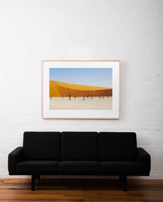 A abstract photo of Africa Landscape in yellow, gol and blue framed in raw timber on white wall above sofa