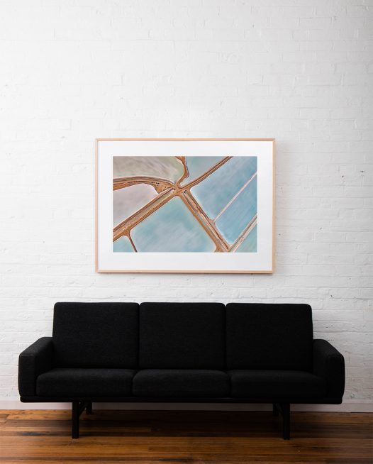 A large abstract aerial photo Water in blue and pink taken in Australia framed in raw timber on white wall above sofa