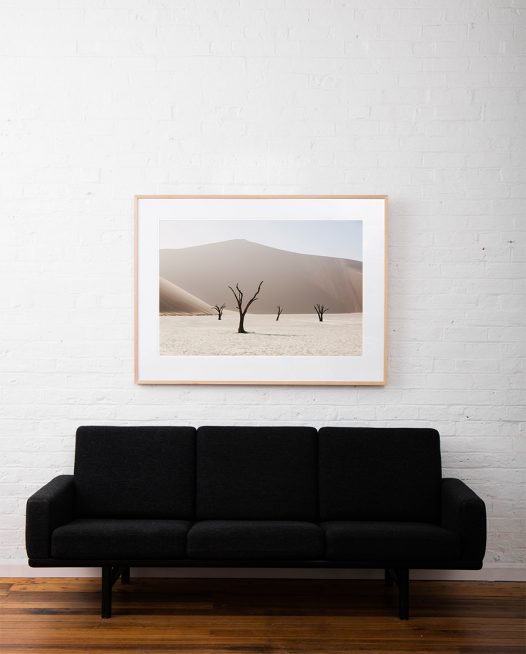 An Abstract photo of African Landscape of mountains, sand and trees in brown, pink and white framed in raw timber on white wall above sofa