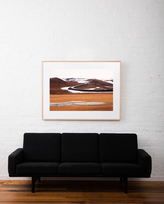 A abstract Iclandic Landscape photo of Mountains and snow in white ,brown and orange framed in raw timber on white wall above sofa