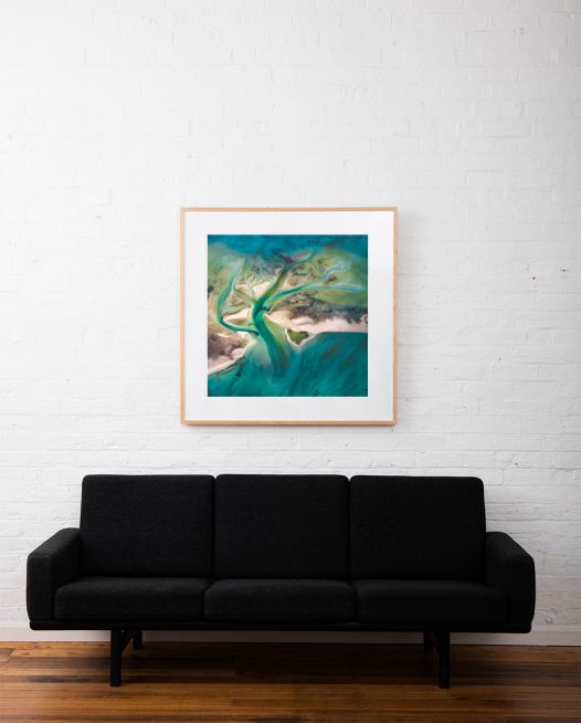 A Abstract Aerial Landscape of water in blue and green framed in raw timber hang on white wall above sofa