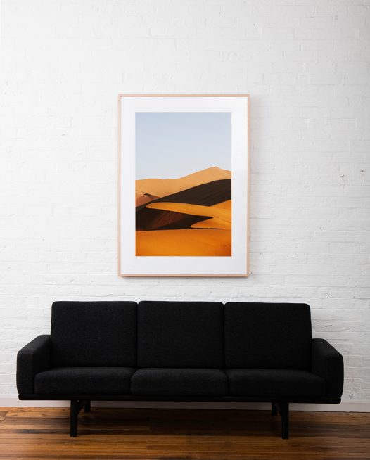 A large vertical abstract photo of African Sand Dunes framed in raw timber on white wall above sofa