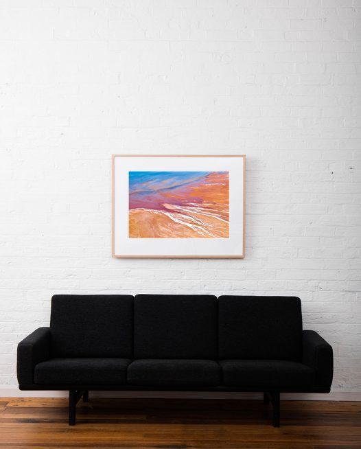 An Abstract Aerial Landscape photo taken in Shark Bay, Australia with splash of colour in orange pink and blue framed raw timber on white wall above sofa