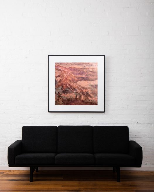 Red and pink aerial photo of the Western Australian landscape print framed in black timber frame on white wall above sofa