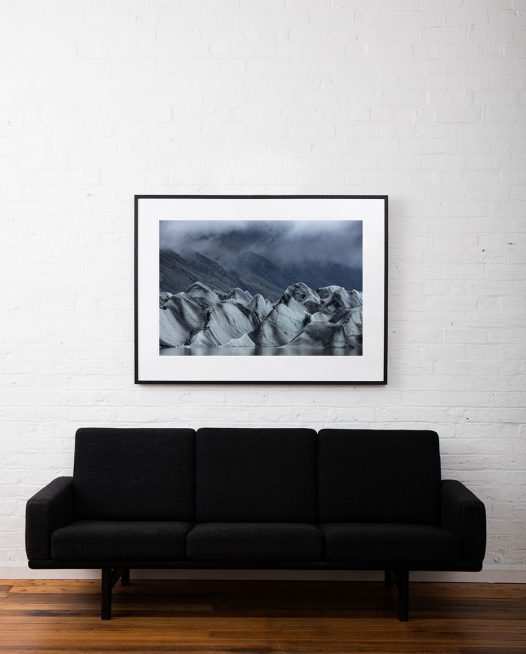 A large horizontal photo of iceberg with mountain background framed in black timber above sofa