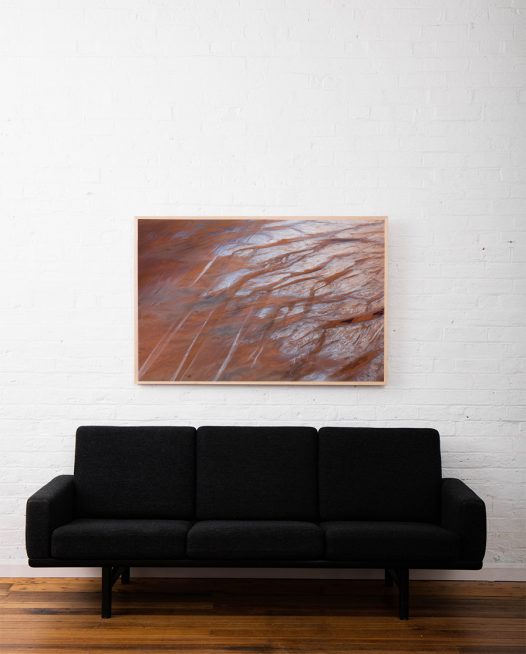 A large aerial photo of inland Australian landscape in brown orange and grey colours framed in raw timber above sofa