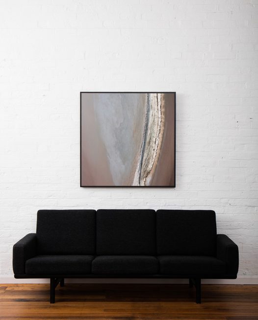 An aerial photo of inland Australian landscape with brown, grey, pink, orange and yellow colour framed in black timber above sofa