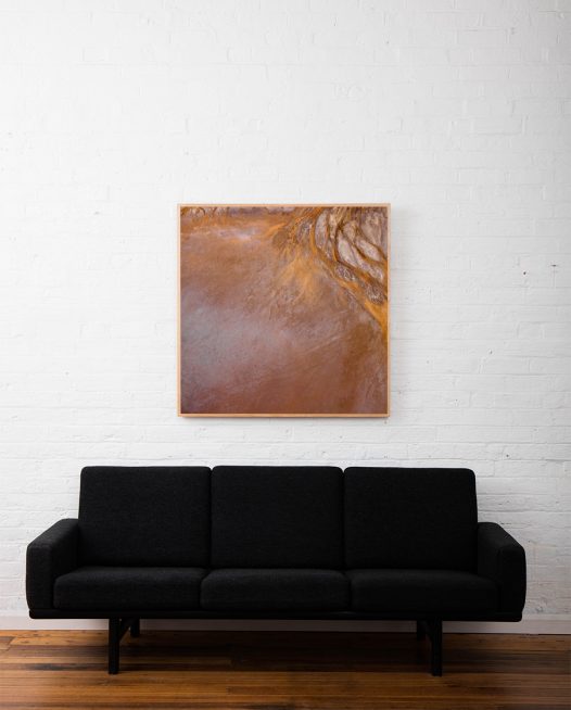 An Aerial photographic print of Lake Eyre in brown and orange colour framed in raw timber above sofa