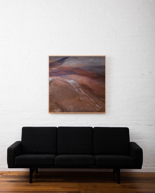 An areial photo of inland Australian landscape of brown, pink, orange, purple colour framed in raw timber above sofa