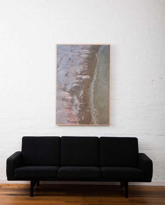 A large aerial photo of inland Australian landscape of pink, grey, brown and orange colour framed in raw timber above sofa